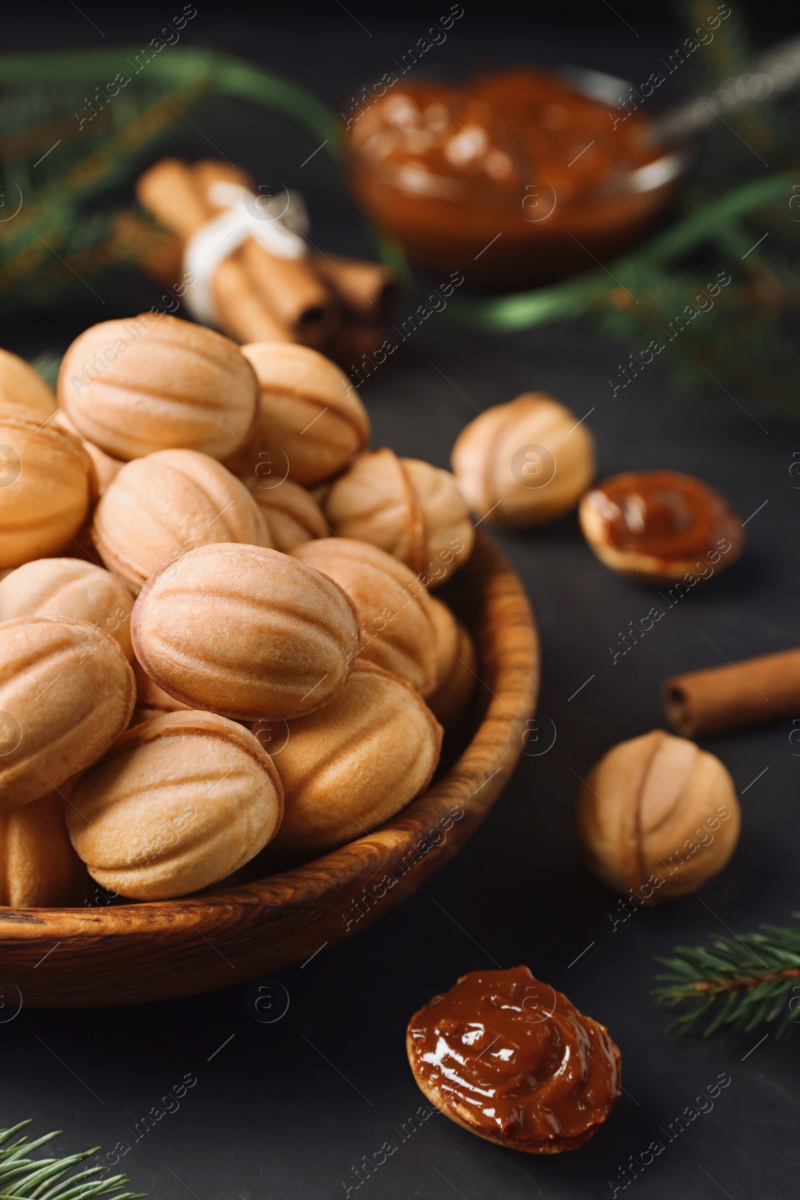 Photo of Homemade walnut shaped cookies with boiled condensed milk, cinnamon stick and fir branches on black table, closeup