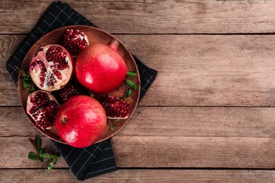 Photo of Delicious ripe pomegranates on wooden table, top view. Space for text