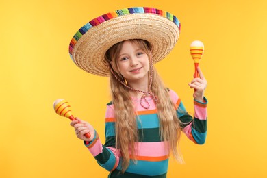 Photo of Cute girl in Mexican sombrero hat with maracas on orange background