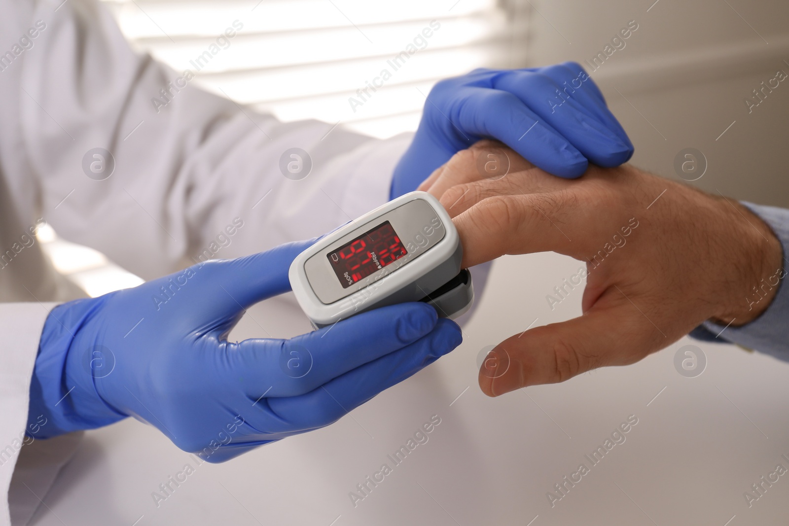 Photo of Doctor checking patient's oxygen level with pulse oximeter at light grey table, closeup