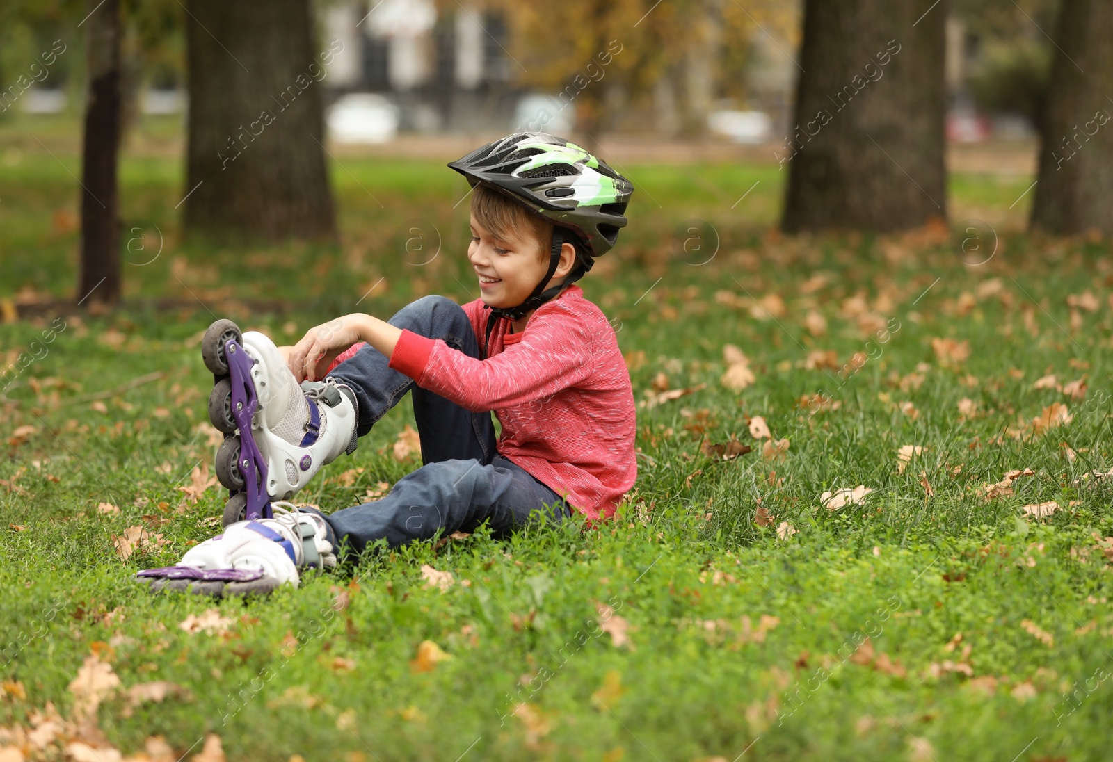 Photo of Cute boy with roller skates sitting on grass in park