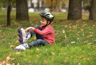 Cute boy with roller skates sitting on grass in park