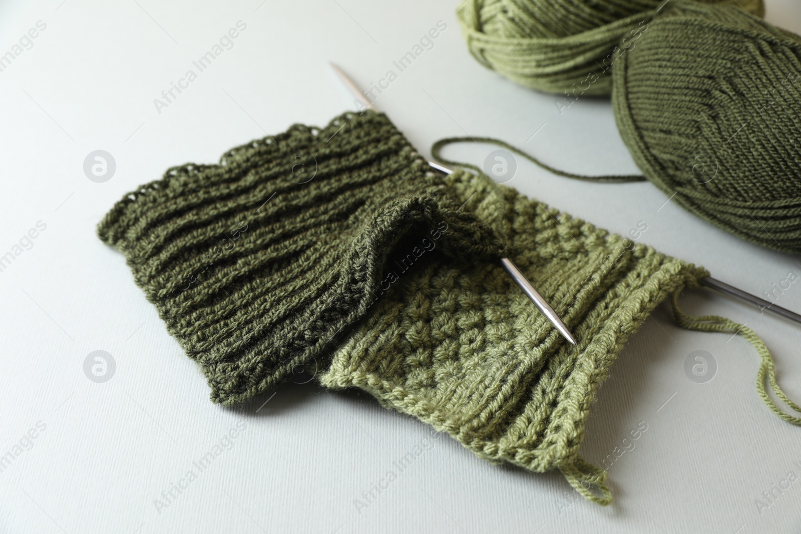 Photo of Green knitting, needles and soft yarns on light background