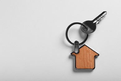 Photo of Key with trinket in shape of house on white background, top view and space for text. Real estate agent services