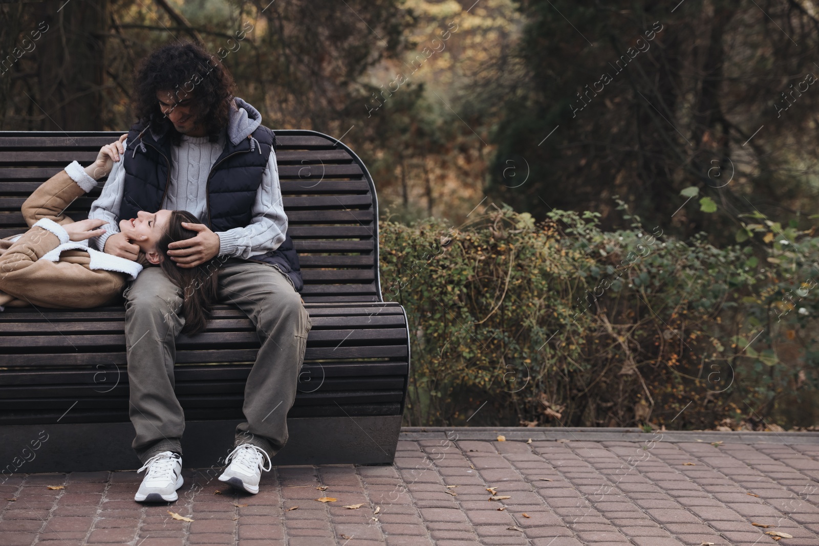 Photo of Happy young couple spending time together on wooden bench in autumn park, space for text. Dating agency