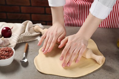 Photo of Woman rolling raw dough at grey table, closeup