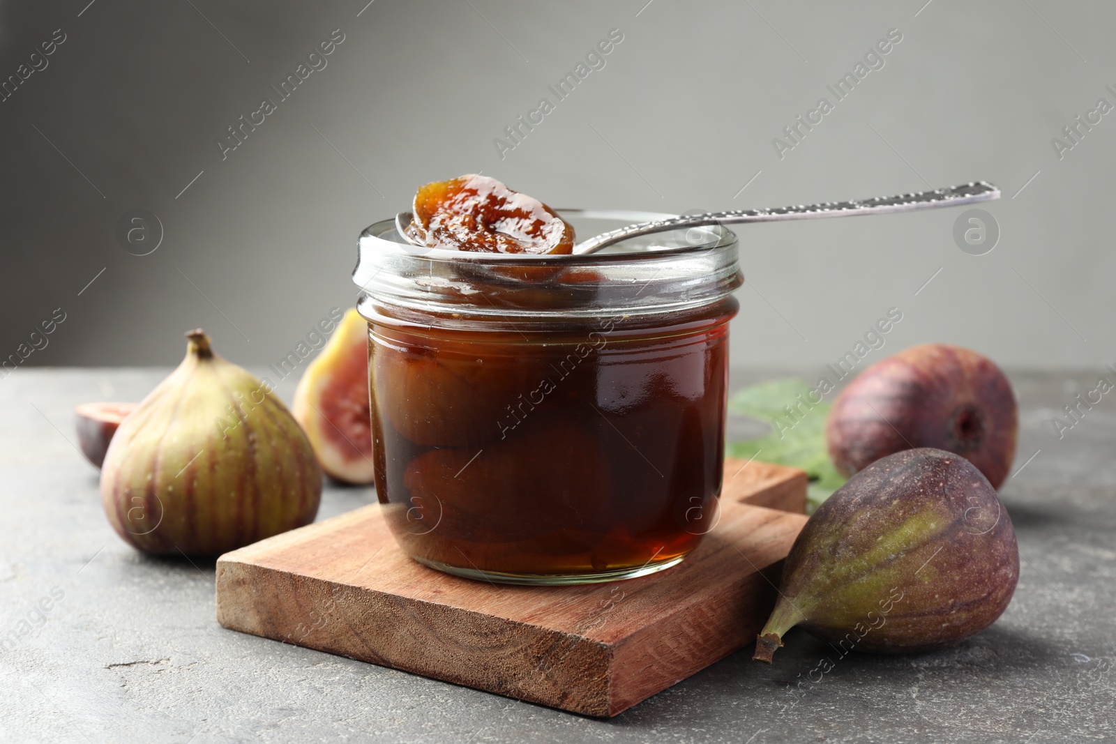 Photo of Jar of tasty sweet jam and fresh figs on grey table