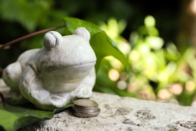 Photo of Frog figure with coins on stone parapet outdoors. Space for text