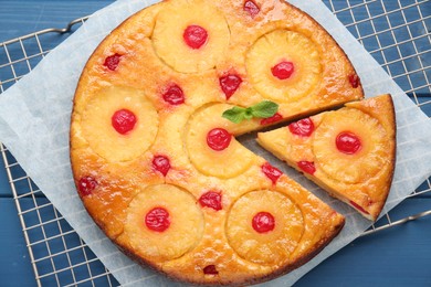 Delicious cut pineapple pie with cherry on blue wooden table, top view