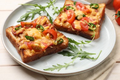 Photo of Tasty pizza toasts and fresh arugula on light wooden table, closeup