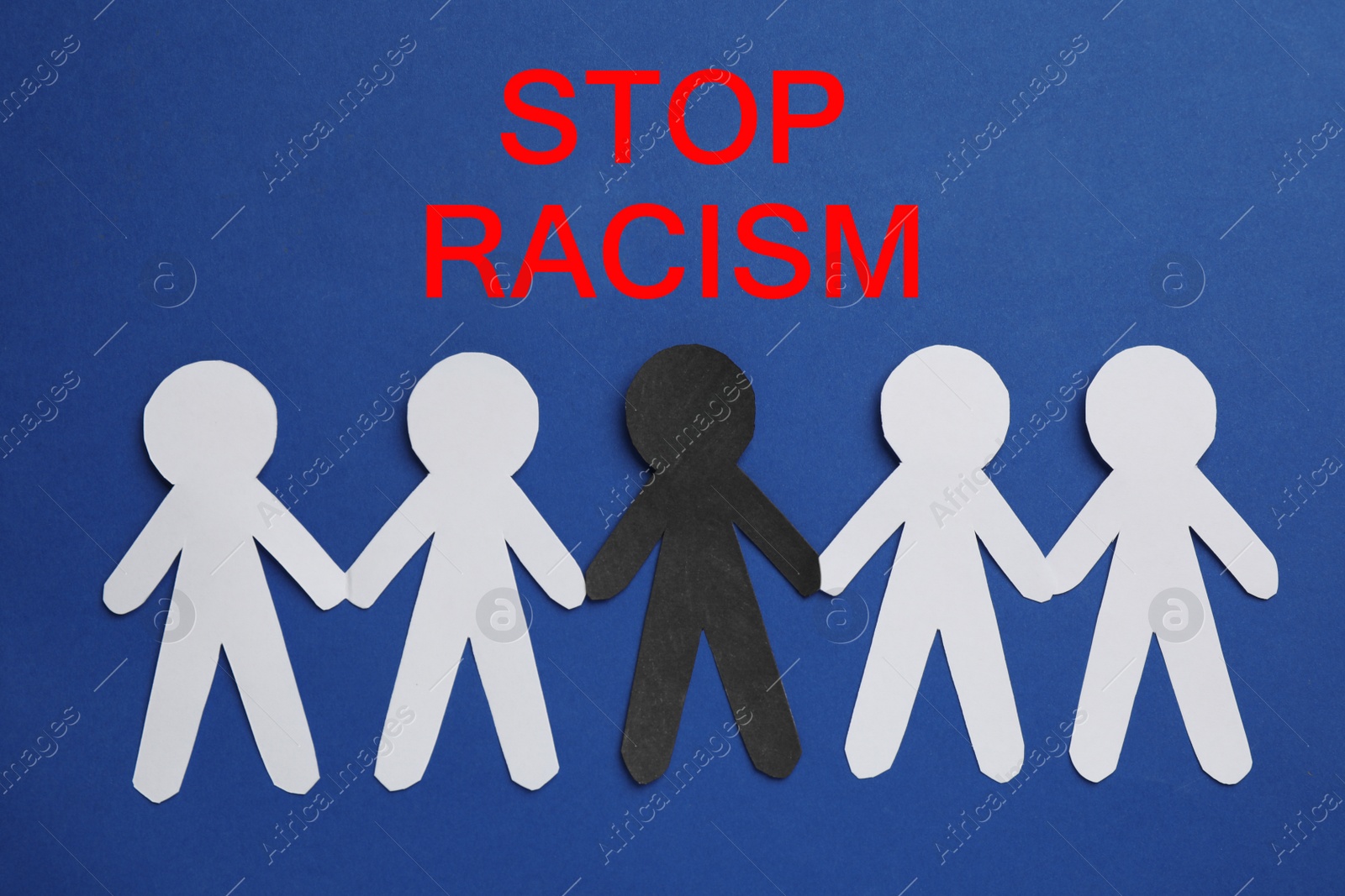 Photo of Words Stop Racism made of cubes near white and black paper humans on blue background, flat lay