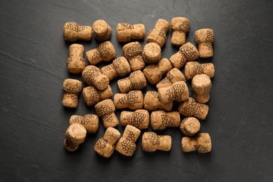 Sparkling wine corks with grape images on black table, flat lay