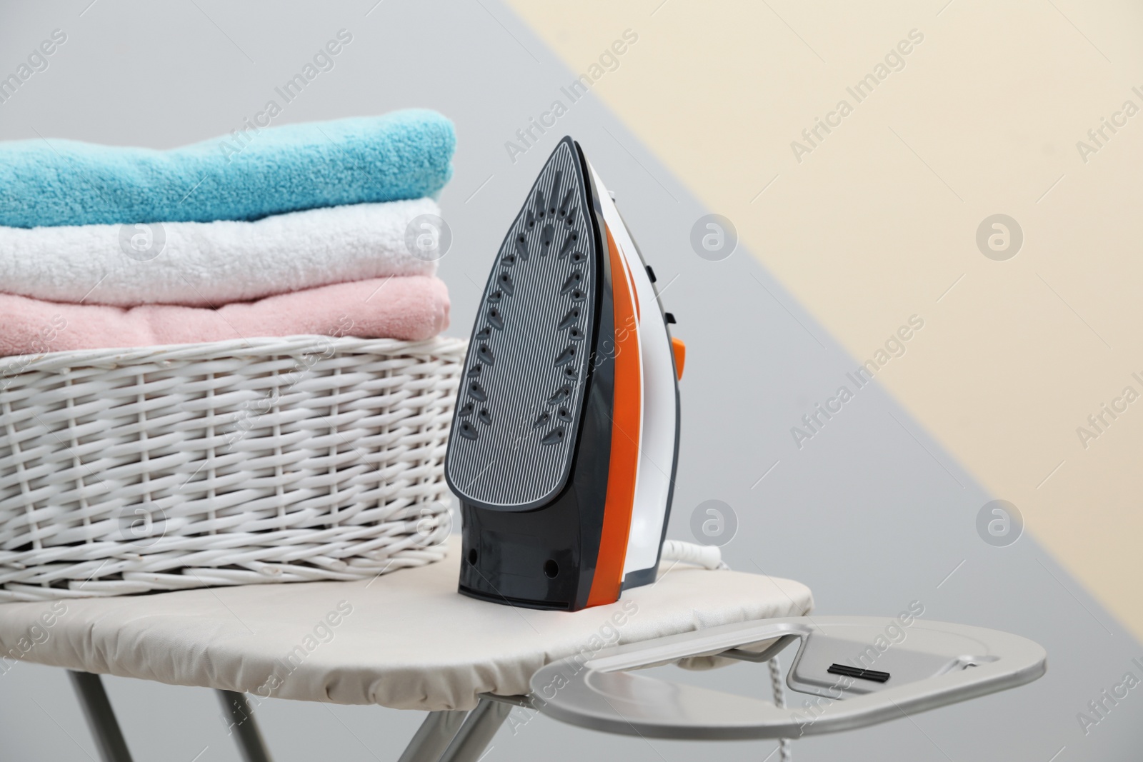 Photo of New modern iron and basket with laundry on board against color background