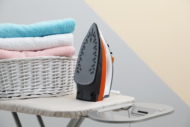 New modern iron and basket with laundry on board against color background