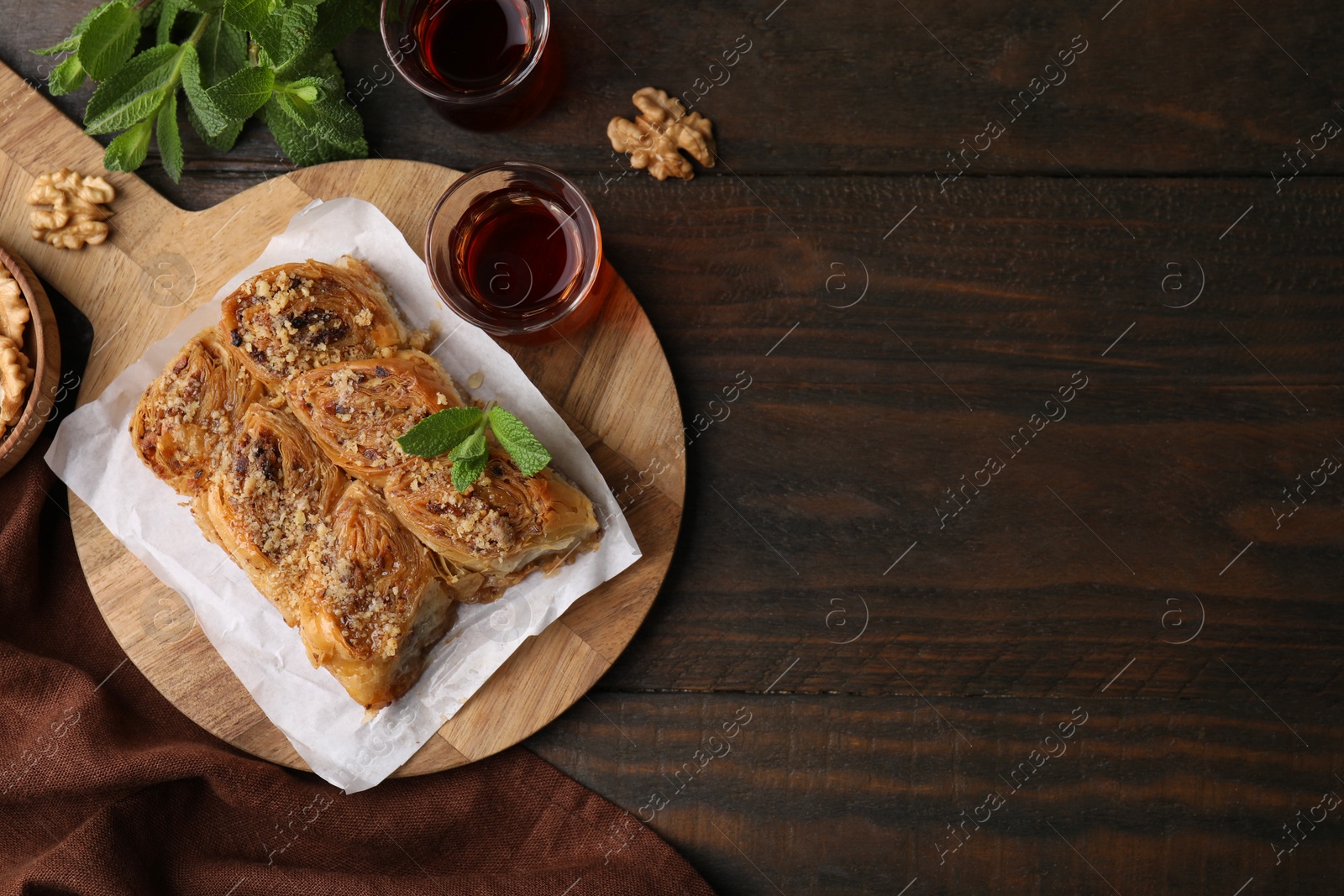 Photo of Eastern sweets. Pieces of tasty baklava, walnuts and tea on wooden table, flat lay. Space for text