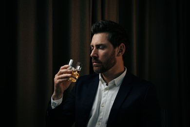 Photo of Man in suit holding glass of whiskey with ice cubes on brown background