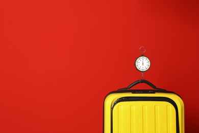 Modern suitcase and hanging scales against color background, space for text