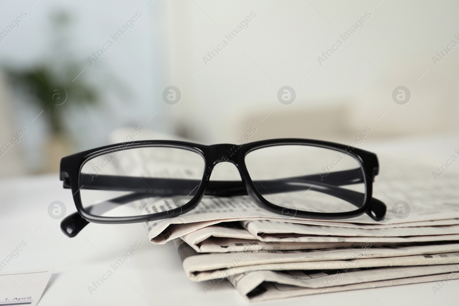 Photo of Stack of newspapers and glasses on white table indoors