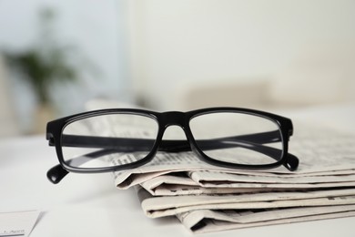 Stack of newspapers and glasses on white table indoors