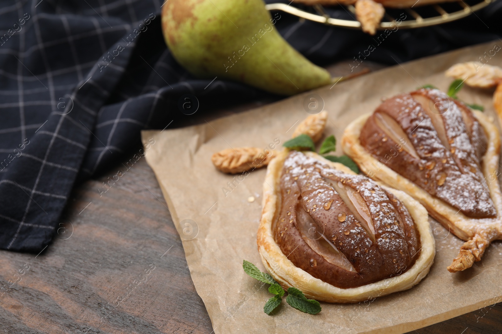 Photo of Delicious pears baked in puff pastry with powdered sugar served on wooden table, closeup. Space for text