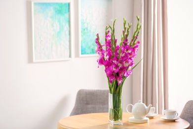 Photo of Vase with beautiful pink gladiolus flowers and tea set on wooden table in room, space for text