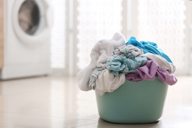 Photo of Plastic basket with dirty clothes on floor in bathroom. Space for text