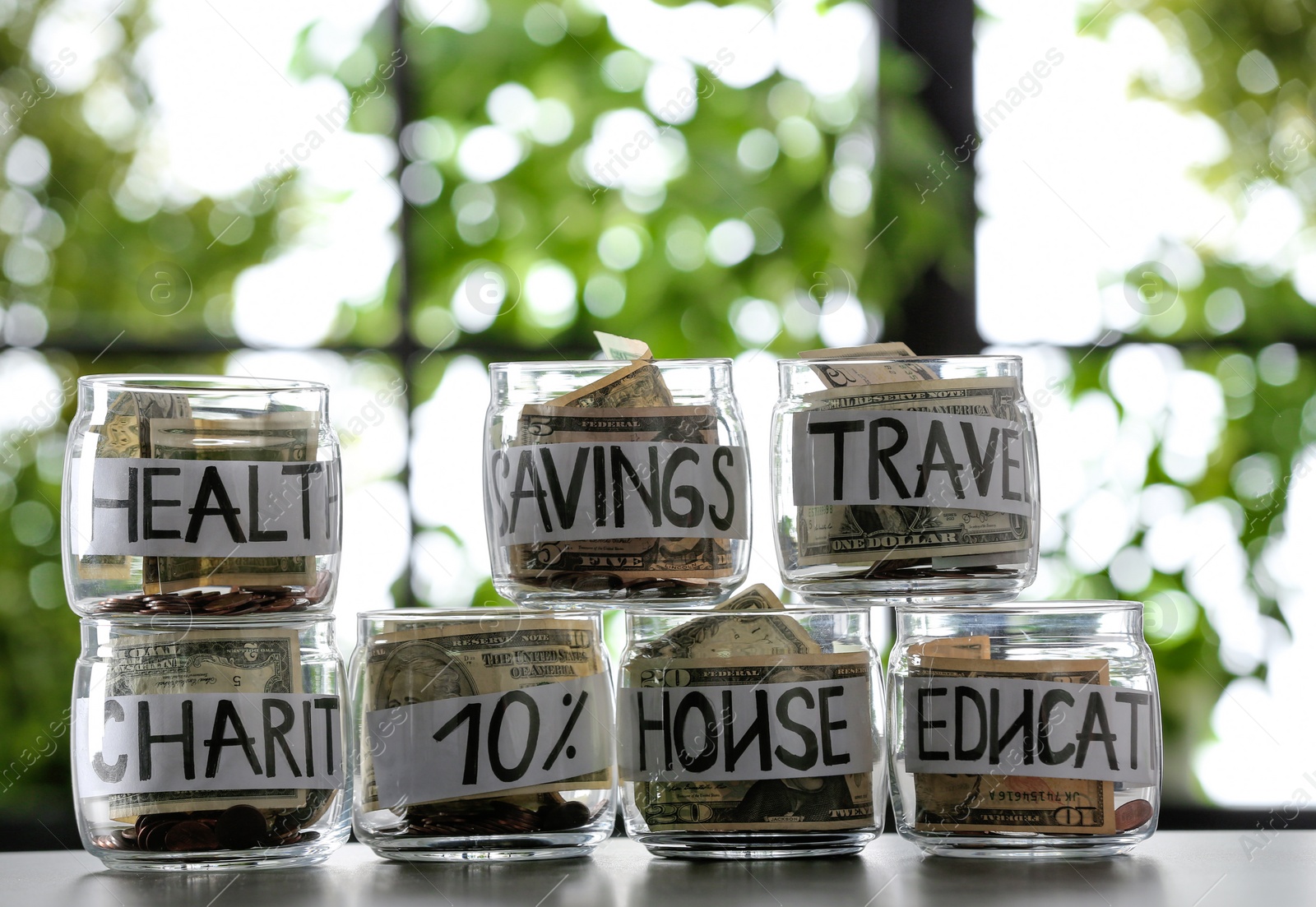 Photo of Glass jars with money for different needs on table against blurred background