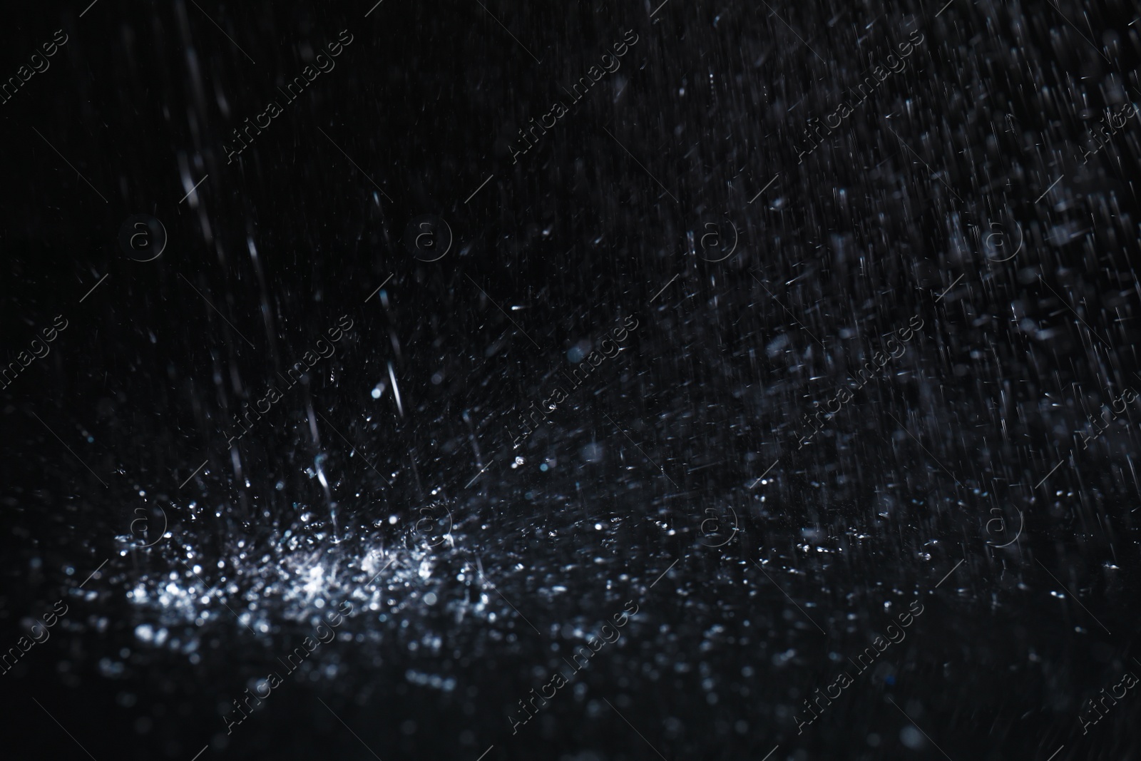 Photo of Heavy rain falling down on ground against dark background, closeup