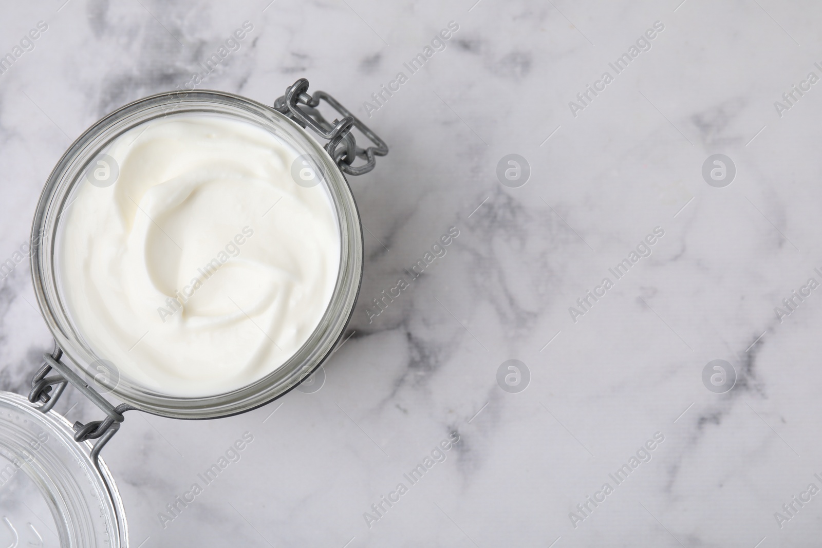 Photo of Delicious natural yogurt in glass jar on white marble table, top view. Space for text