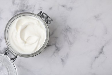 Photo of Delicious natural yogurt in glass jar on white marble table, top view. Space for text