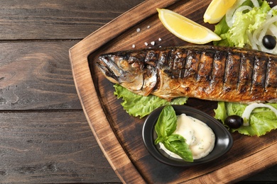 Wooden board with delicious grilled fish on table, top view