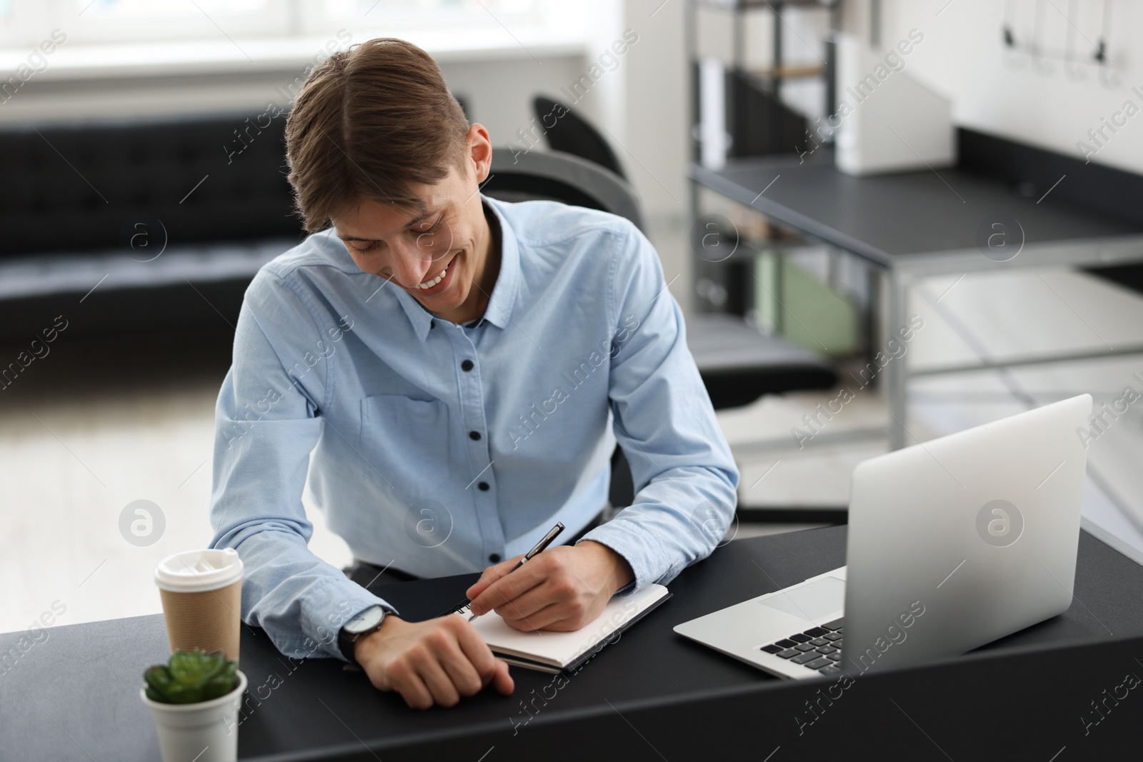 Photo of Man taking notes during webinar at table in office