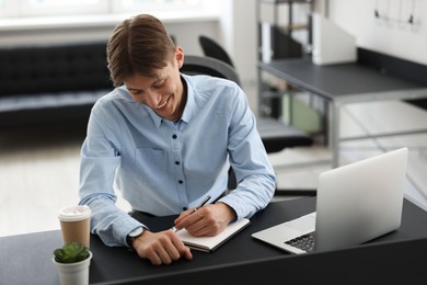 Man taking notes during webinar at table in office