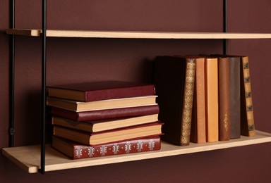 Photo of Shelves with different books on brown wall, closeup