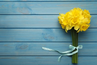 Beautiful daffodil bouquet on blue wooden table, top view. Space for text