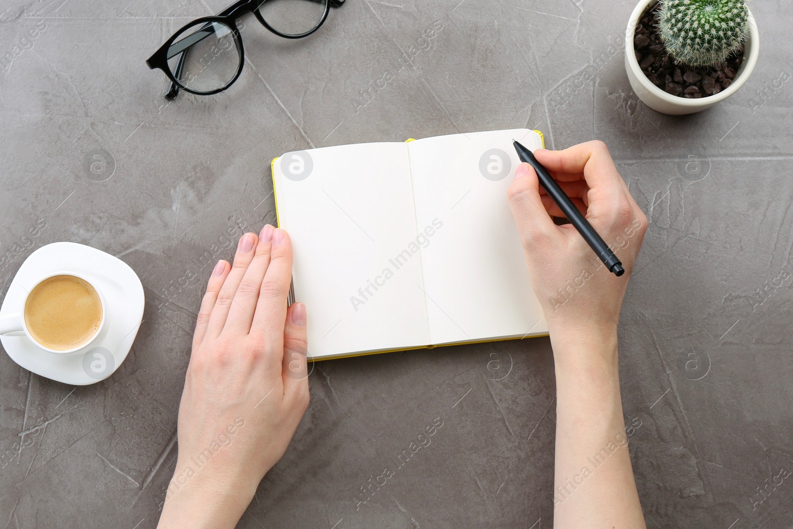 Photo of Woman writing in notebook at grey table, top view