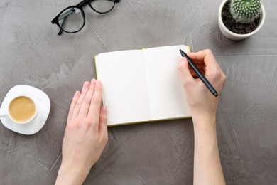 Woman writing in notebook at grey table, top view