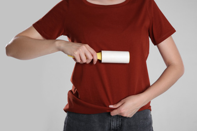 Photo of Woman cleaning red t-shirt with lint roller on grey background, closeup