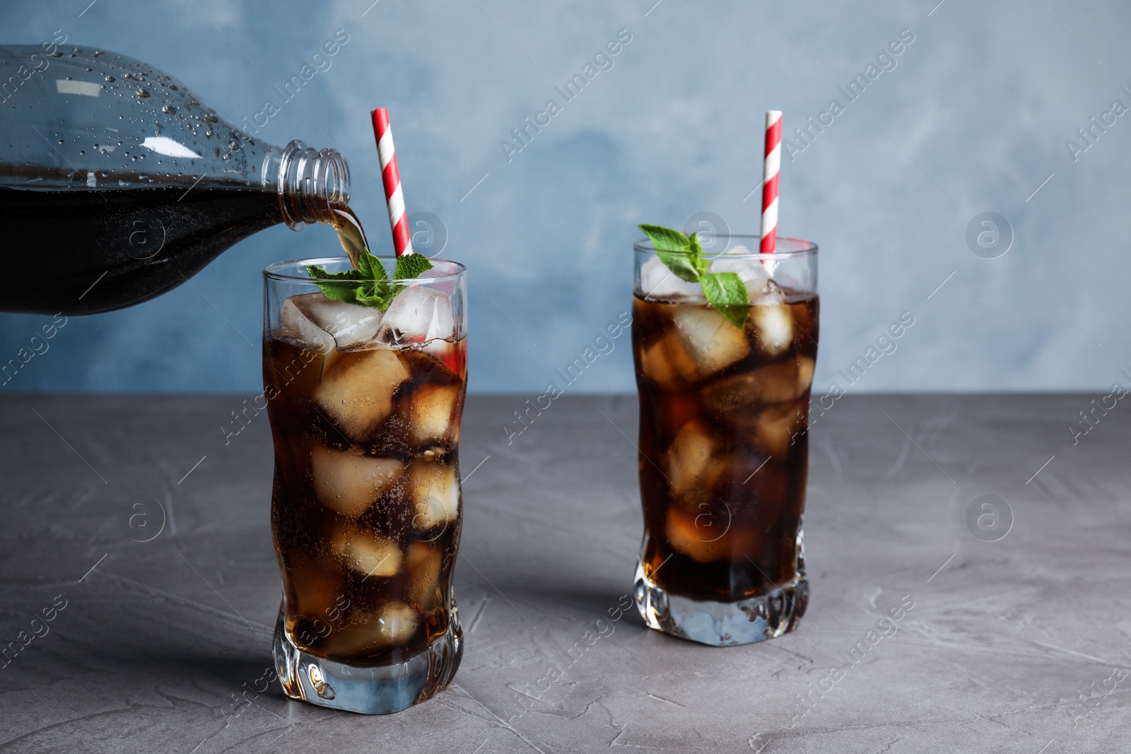 Photo of Pouring refreshing soda drink into glass on grey table against blue background