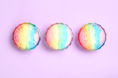 Photo of Rainbow shaving ice in glass dessert bowls on lilac background, flat lay