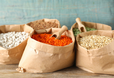 Photo of Different grains and cereals in paper bags on wooden table