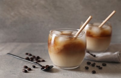 Photo of Refreshing iced coffee with milk in glasses, beans and spoon on gray table, closeup. Space for text