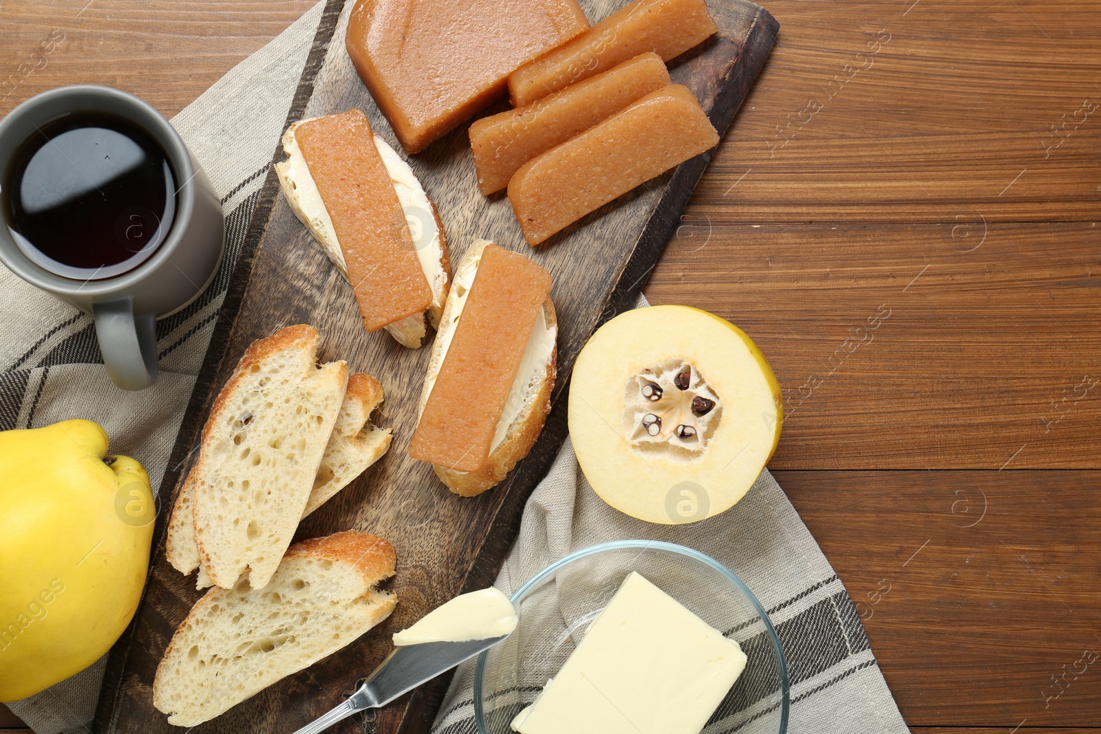 Photo of Delicious quince paste, bread, butter, cup of tea and fresh fruits on wooden table, flat lay. Space for text