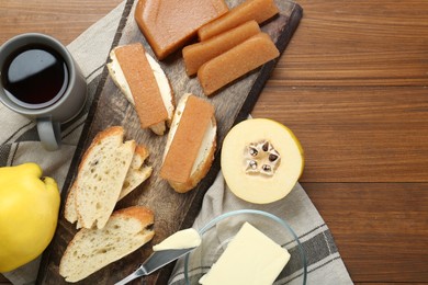 Photo of Delicious quince paste, bread, butter, cup of tea and fresh fruits on wooden table, flat lay. Space for text