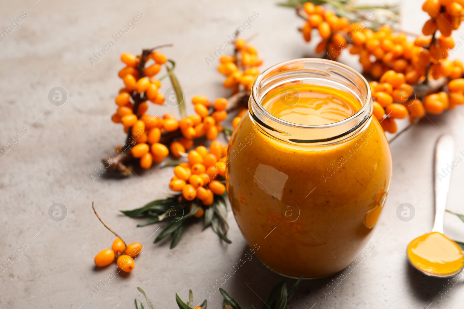 Photo of Delicious sea buckthorn jam and fresh berries on grey table. Space for text