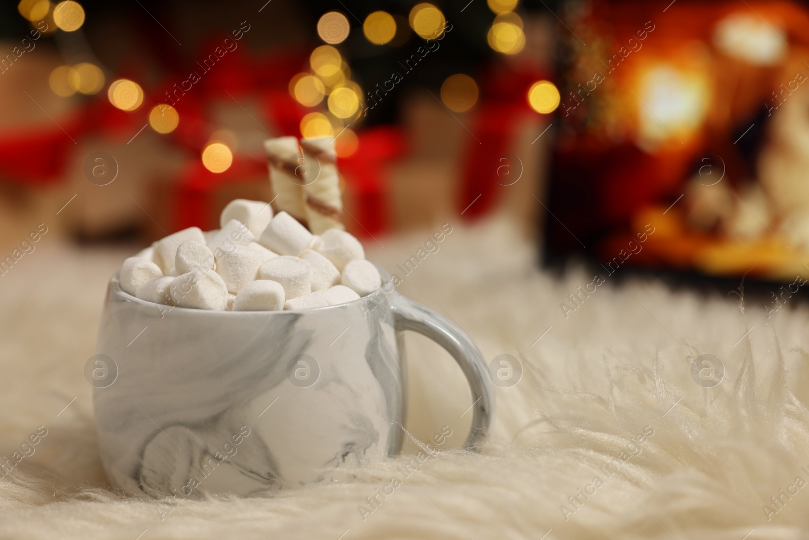 Photo of Christmas cocoa with marshmallows and wafer sticks in cup on soft carpet indoors, closeup. Space for text