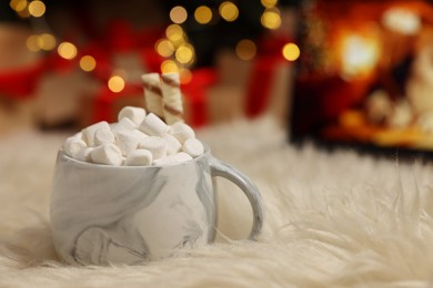 Photo of Christmas cocoa with marshmallows and wafer sticks in cup on soft carpet indoors, closeup. Space for text