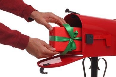 Photo of Man putting Christmas gift into mailbox on white background, closeup. Sending present by mail