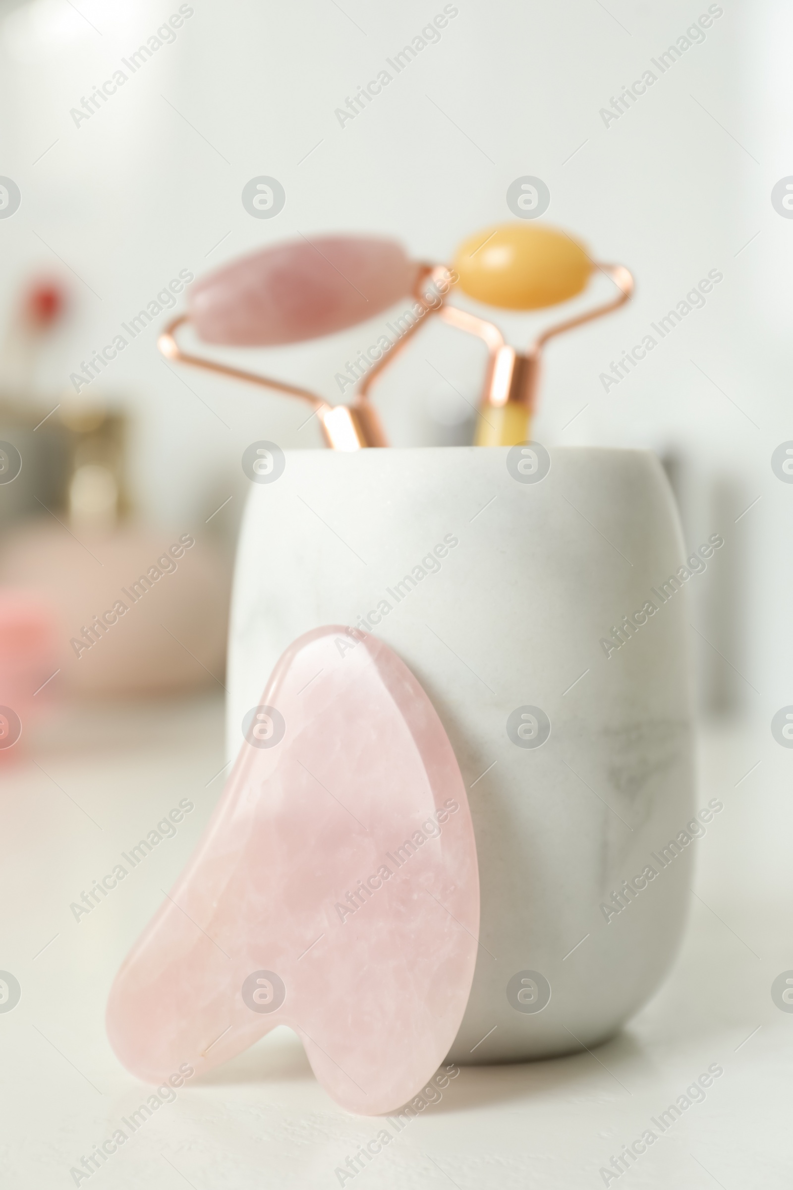 Photo of Rose quartz gua sha tool near holder with natural face rollers on white table