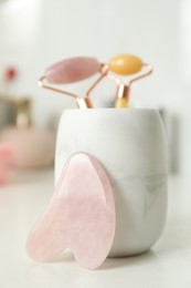 Rose quartz gua sha tool near holder with natural face rollers on white table